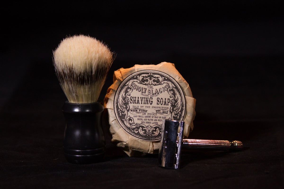 Shaving brush, soap, and safety razor on black background